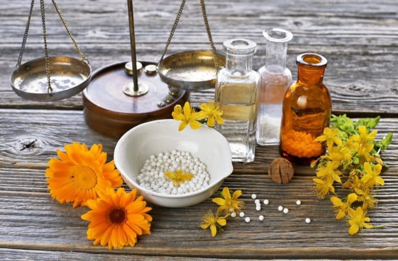 Homeopatické kuličky v misce, tinktury a léčivé květiny na dřevěném stole